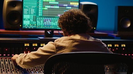 Cheerful energic audio engineer dancing on his own music creation in professional studio, editing a...
