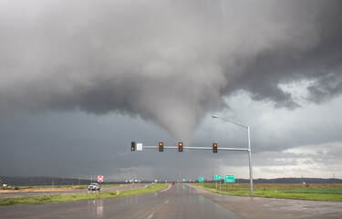 A tornado crosses the road up ahead beyond a traffic light.