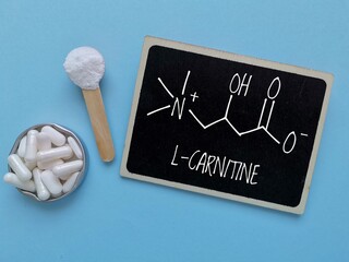 Structural chemical formula of L-carnitine with white tablets and L-carnitine powder. L-carnitine is an amino acid produced by the body, also found in supplements, helps the body turn fat into energy.