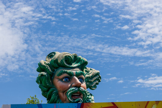 The entrance to Blaine Kerns Mardi Gras World with a parade float of a man with green hair lush green trees and grass, blue sky and clouds in New Orleans Louisiana USA