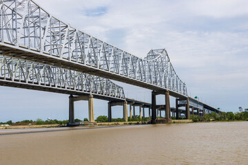The Crescent City Connection bridge over the Mississippi River with lush green trees, plant and...