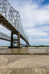 The Crescent City Connection bridge over the Mississippi River with lush green trees, plant and grass, a boat sailing on the water, blue sky and clouds in New Orleans Louisiana USA