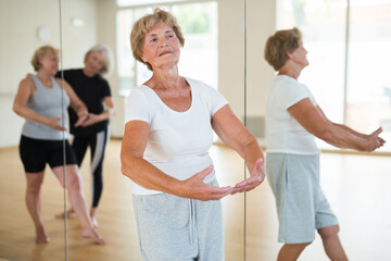 Elderly women who are engaged in the dance section at a group lesson stand in the 1st position of...