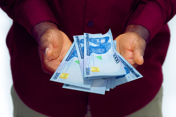 Black man in red long sleeve shirt holding 1000 Nigerian Naira notes with opened palms

