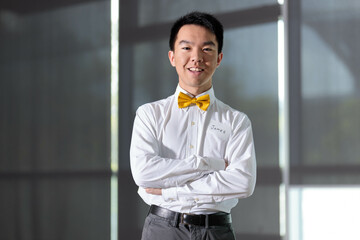 Young man with name tag in white dress shirt and yellow bow tie, arms crossed portrait