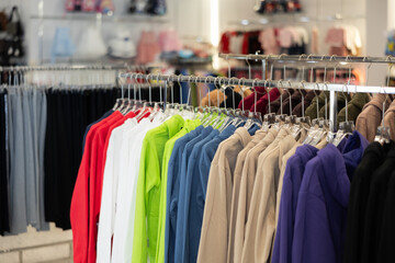 Different hoodies hanging on stand in big clothing store with large assortment