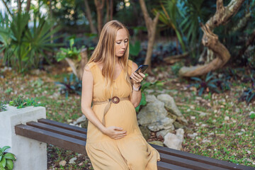 pregnant woman enjoys the tranquility of the park, captivated by her phone, blending the beauty of nature with the modern connection during her pregnancy