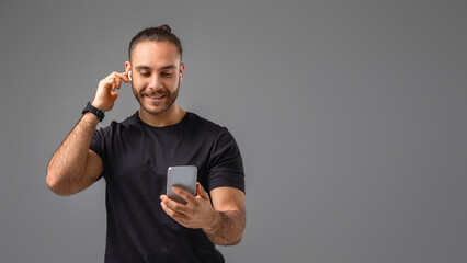 Man in Black Shirt Holding Smart Phone, Touching Earbud