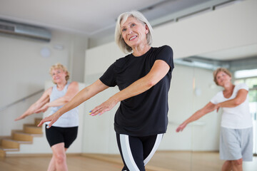 Positive senior women in sportswear dancing in fitness room.