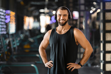 Fototapeta premium Handsome Millennial Man With Headphones Standing in Gym