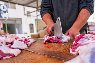A man with a focused expression carefully slices through a piece of meat on a sturdy wooden cutting...