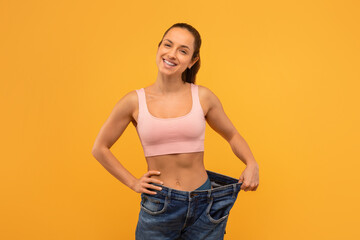 Smiling Young Woman Demonstrating Weight Loss by Holding Oversized Jeans