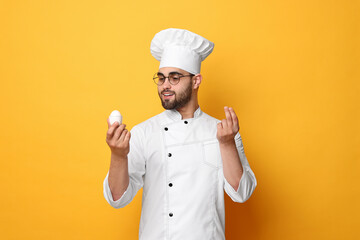 Professional chef holding egg and showing perfect sign on yellow background
