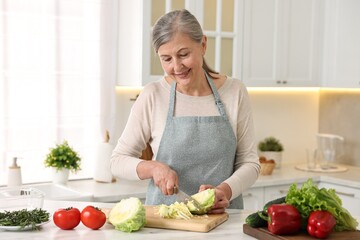 Happy housewife cutting cabbage at table in kitchen