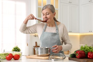 Housewife with spoon cooking at table in kitchen