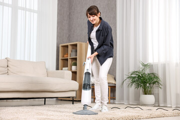 Happy young housewife vacuuming carpet at home