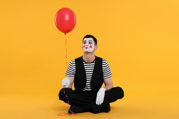 Funny mime artist with balloon on orange background