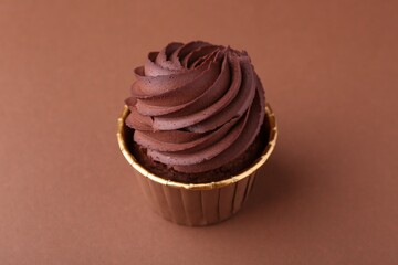 Delicious chocolate cupcake on brown background, closeup