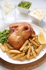 Tasty fish, chips, sauce, peas and lemon on white wooden table, closeup