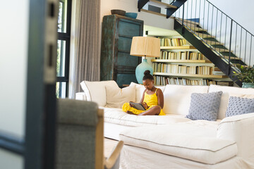 African American girl in yellow dress, reading at home on white sofa