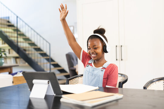 African American girl with headphones raises hand in tablet-based online lesson