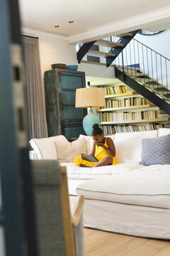 African American girl in yellow dress, reading at home on white couch
