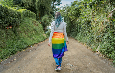 mujer joven de cabello largo usando en su cadera la bandera gay mientras camina al aire libre 