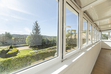A closed terrace with large aluminum and glass windows with good views of the mountains with trees...