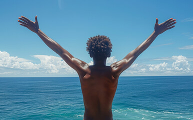 Back shot of an African-American man naked from the waist up with his arms raised looking out to sea