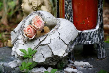 a crumbling stone heart with roses on a abandoned grave in a cemetery