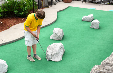 Young man playing mini golf on putting green - obrazy, fototapety, plakaty
