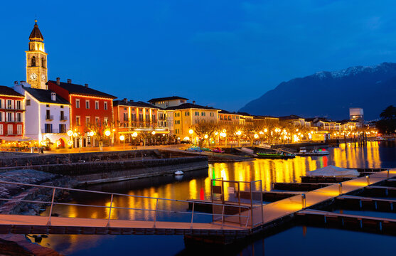 View of embankment in Ascona, canton of Ticino, Switzerland. Houses along waterfront, turned on city lights in evening.