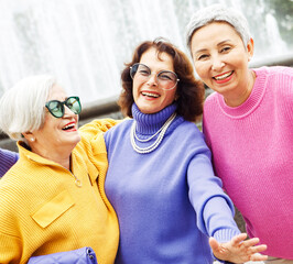 Three happy cheerful pensioner female friends in bright sweaters and sunglasses walk together