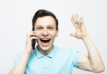 Happy young man holding a phone to his ear, listening to the news. - obrazy, fototapety, plakaty