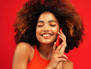 Portrait of an excited young afro american woman talking on mobile phone over red background