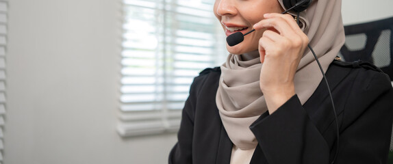 Call center worker, young Muslim woman wearing hijab, talking to customer on call phone on computer...