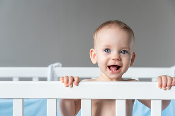 A baby laughing out loud reaches out from his crib with his hand