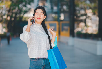 A woman is talking on her cell phone while holding a blue shopping bag