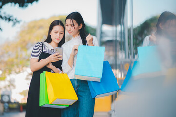 Two women are looking at their cell phones while holding shopping bags