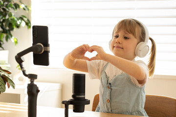 Young podcaster making heart shape with hands, joyfully recording. Blogging and podcasting.