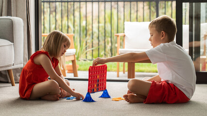 Siblings engrossed in a strategic board game, enhancing their logic. Kids play board games - four...
