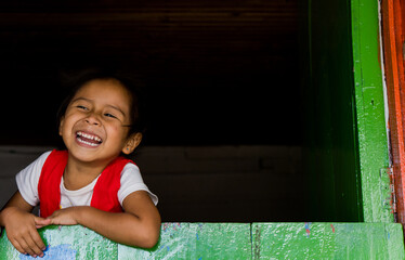 niña pequeña sonriendo feliz mientras esta asomada por una ventana de su casa 