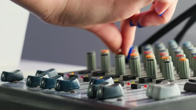 Skilled woman musician engages in adjusting settings on mixing console in studio. Female hand turns buttons and rotary knobs slow motion