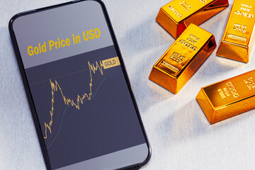  application with gold price information on screen of smartphone and gold bars.