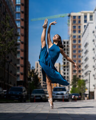 Fototapeta na wymiar Beautiful Asian ballerina in blue dress posing in splits outdoors. Urban landscape. Vertical photo. 