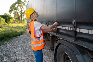 Woman driver with hard hat checking trailer on her truck 