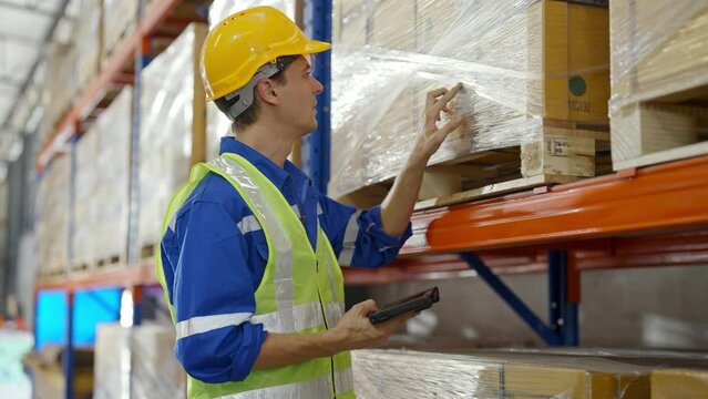Young caucasian man warehouse workers holding digital tablet checking inventory management packaging boxes. Man staff wearing vest and safety helmet and walking count the box at storehouse - Powered by Adobe