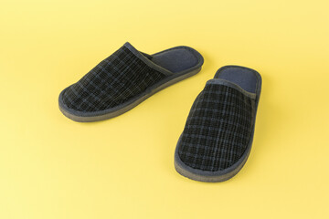 A pair of men's home slippers on a yellow background.