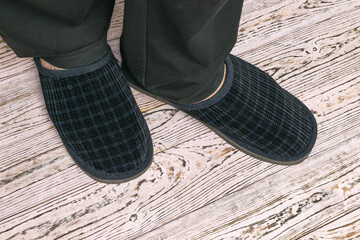 Men's feet in slippers on a wooden background.