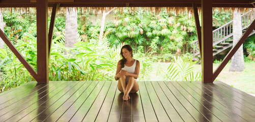 Young and beautiful woman in white swimsuit. Woman posing in exotic Thai bungalow. Resting and...